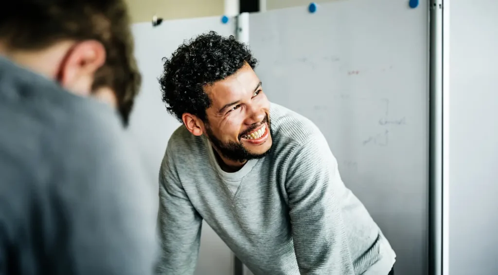 candid image of two people working, the main person in focus is a black young professional that is smiling and looking outside the frame